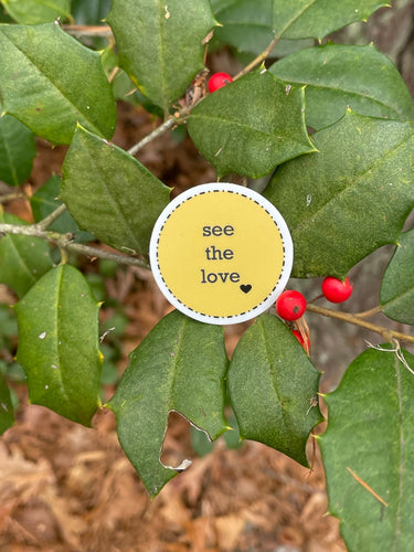 yellow, 1.5', round sticker with white border and black message, see the love, with a small black heart at the bottom right of the letters 