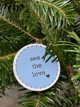 Load image into Gallery viewer, light blue, 1.5&#39;, round sticker with white border and black message, see the love, with a small black heart at the bottom right of the letters 
